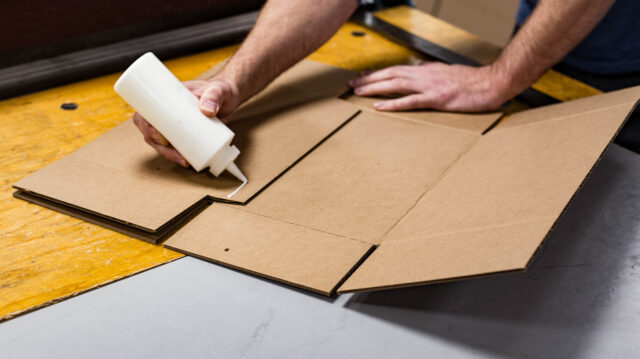 A man using a glue stick to construct a cardboard box.