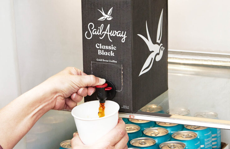 A person pouring a cup of coffee from a box in a fridge.