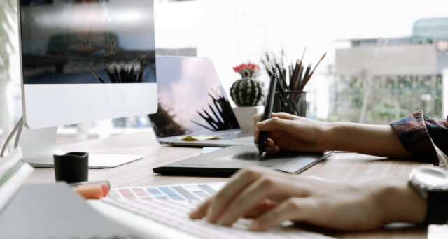 A person working at a desk with a computer and a pen.