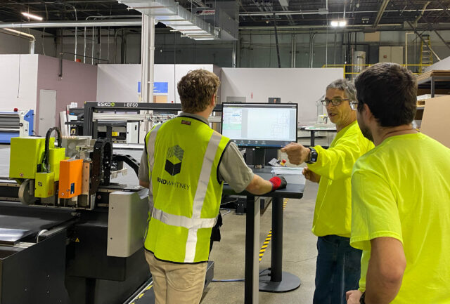 A group of people standing around a machine in a factory.