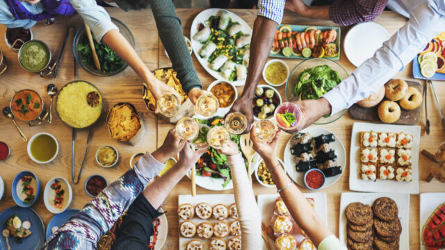 A group of people toasting around a table full of food.