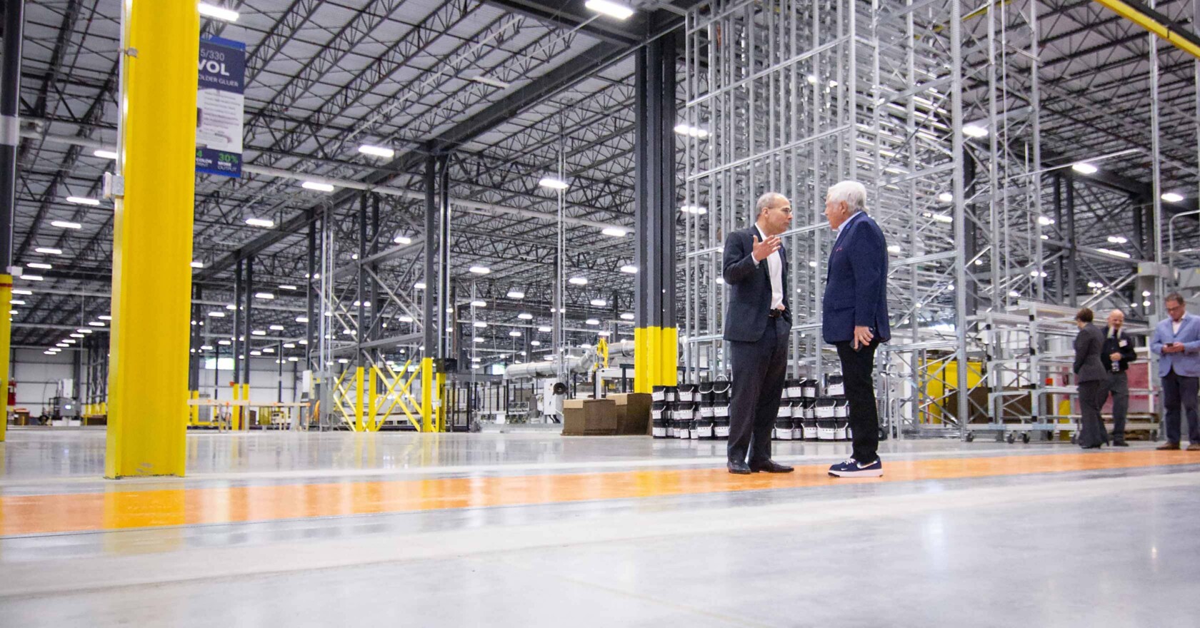 Two men standing in a warehouse talking to each other.